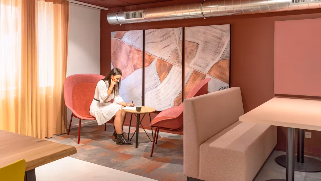 Image of a women sat at a coffee table with a Rockfon Canva acoustic canvas on the wall.