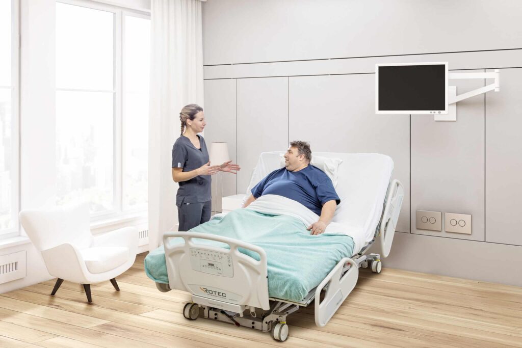 Image of a patient in a bariatric bed in conversation with a nurse.